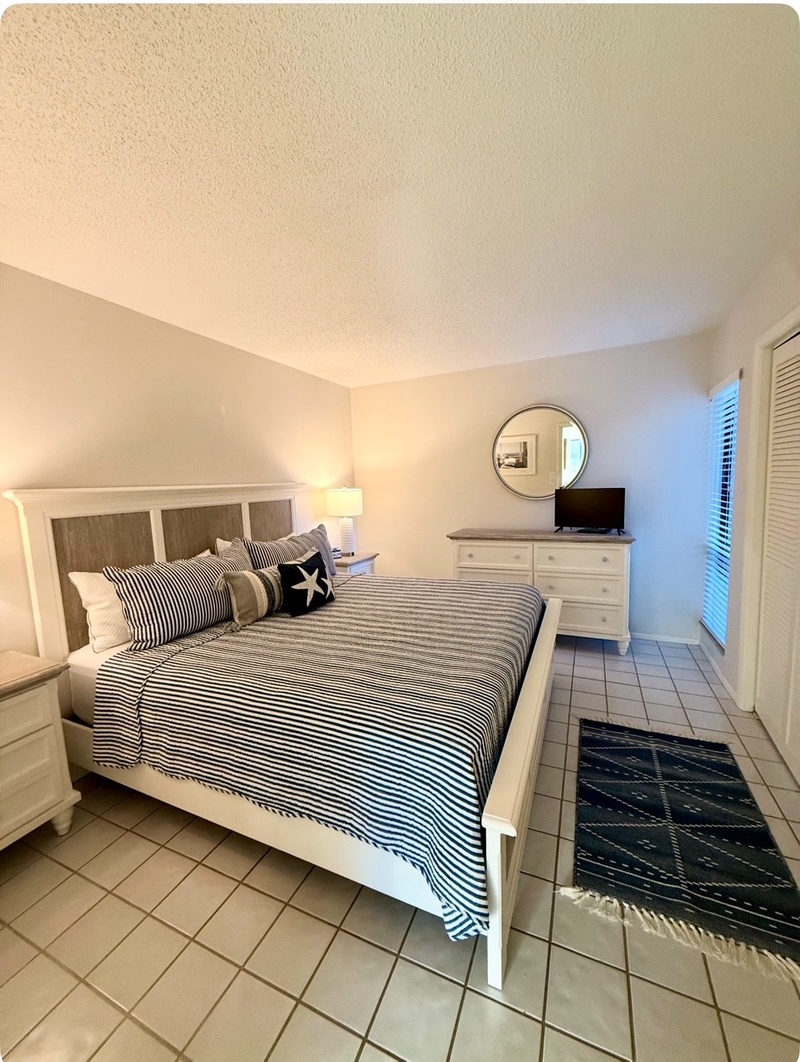 Drift off in your comfortable bedroom with crisp nautical bedding and peaceful natural light streaming through the window.