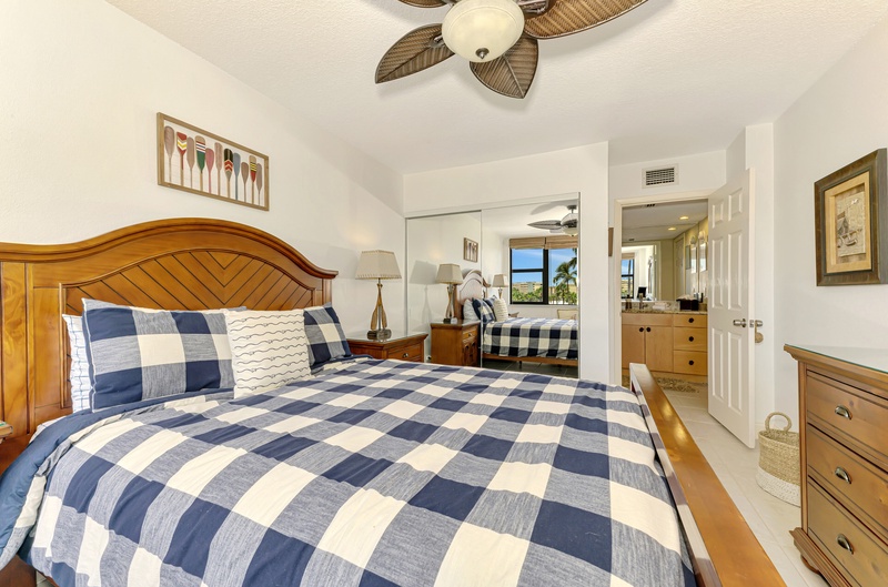 Drift off in your cozy bedroom with tropical ceiling fan, warm wood furnishings, and cheerful blue-checkered bedding that invites peaceful rest.