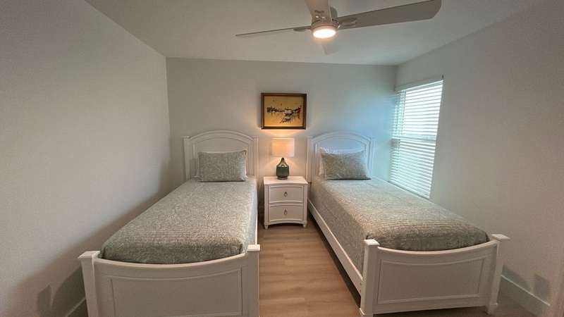 Rest peacefully in your twin bedroom with matching white beds, soft gray linens, and gentle ceiling fan breeze.