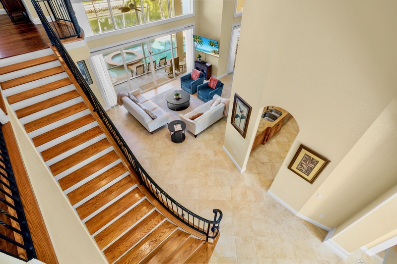 Descend the elegant curved staircase into your spacious living area, where modern comfort meets luxury with soaring ceilings and pool views.
