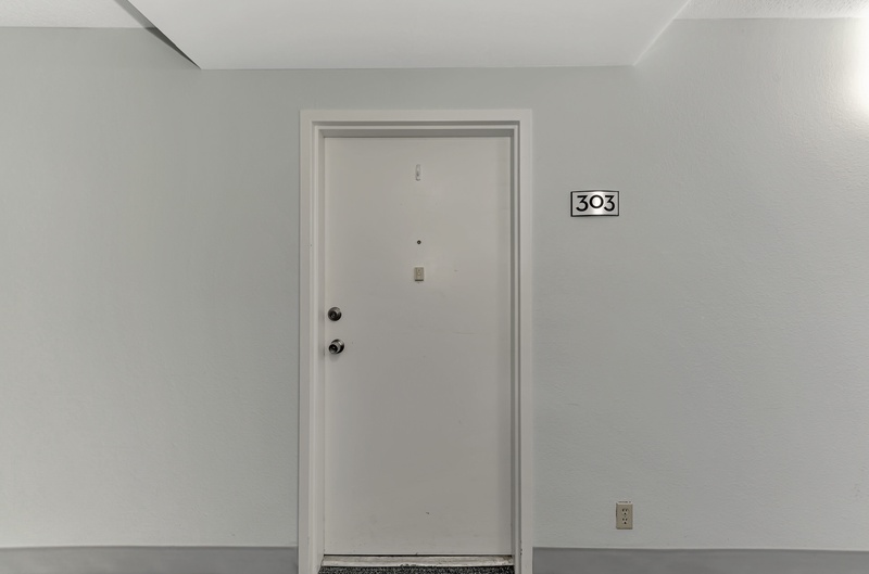 Clean hallway entrance to room 303 with modern finishes and secure entry.