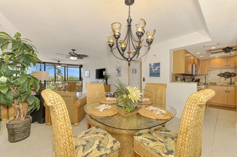 Relax in your tropical dining space with wicker chairs and glass table, while natural light streams through windows overlooking palm trees.