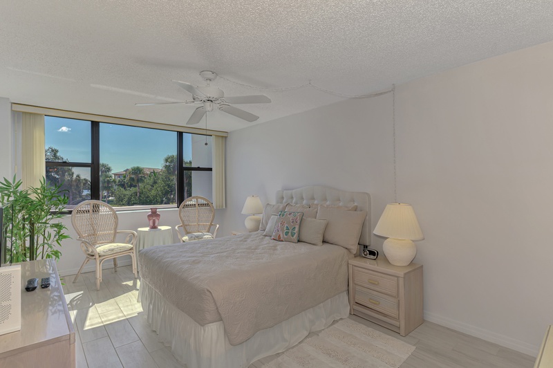 Your peaceful bedroom retreat features a cozy queen bed, ceiling fan, and large windows overlooking tropical gardens.