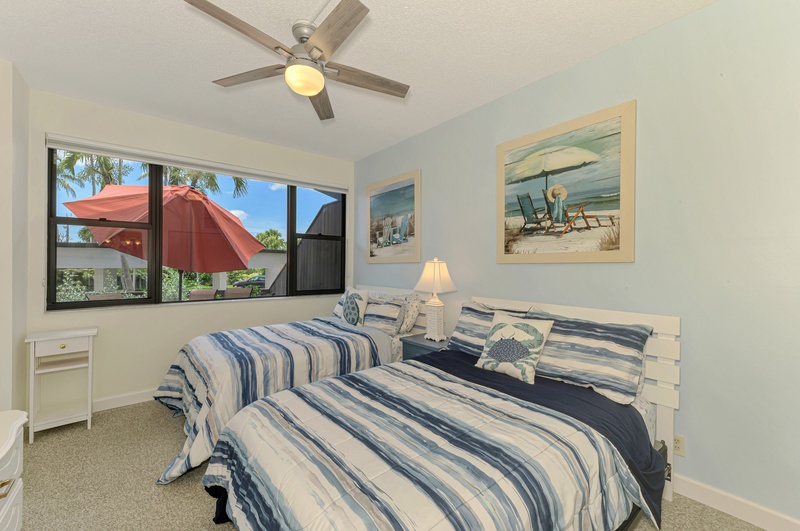 Your coastal bedroom features twin beds with beach-themed decor, a ceiling fan for comfort, and cheerful views of the tropical outdoors.