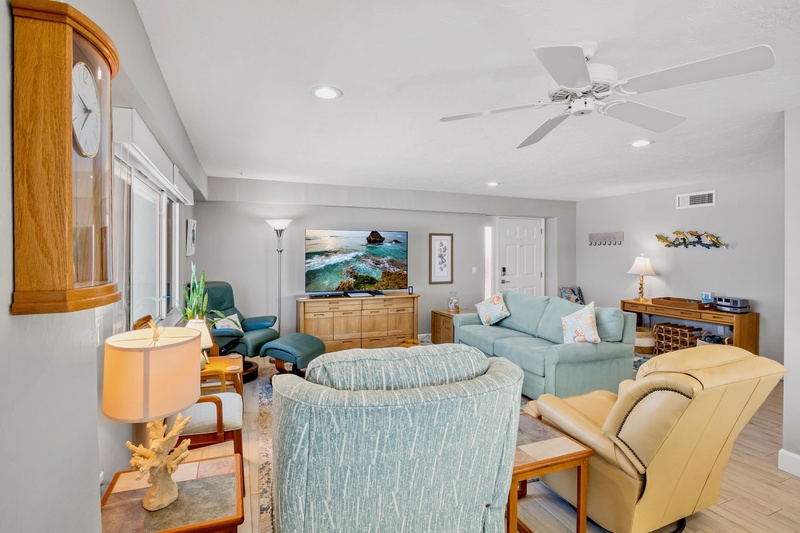 Relax in your spacious living room with coastal decor, ceiling fan, and comfortable seating perfect for unwinding after beach days.