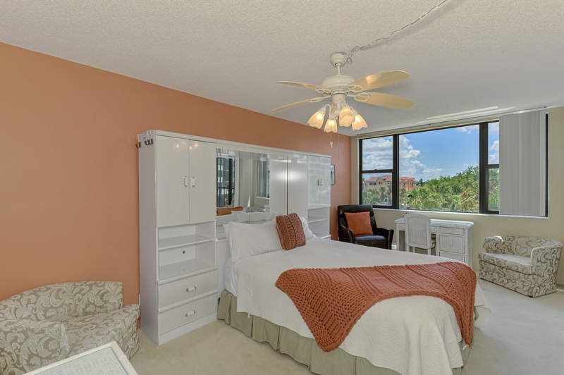 Your bright bedroom features warm coral accents, built-in storage, and stunning garden views through floor-to-ceiling windows.