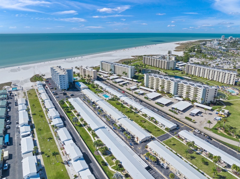 Aerial view of beachfront vacation rental community with pristine white sand beach and turquoise waters stretching to the horizon.