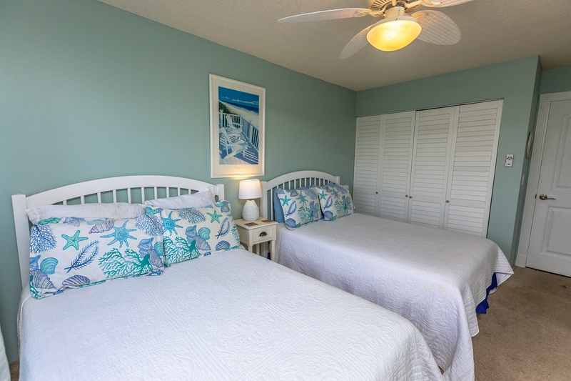 Your coastal-themed bedroom features two comfortable beds with ocean-inspired pillows, creating a serene retreat after beach adventures.