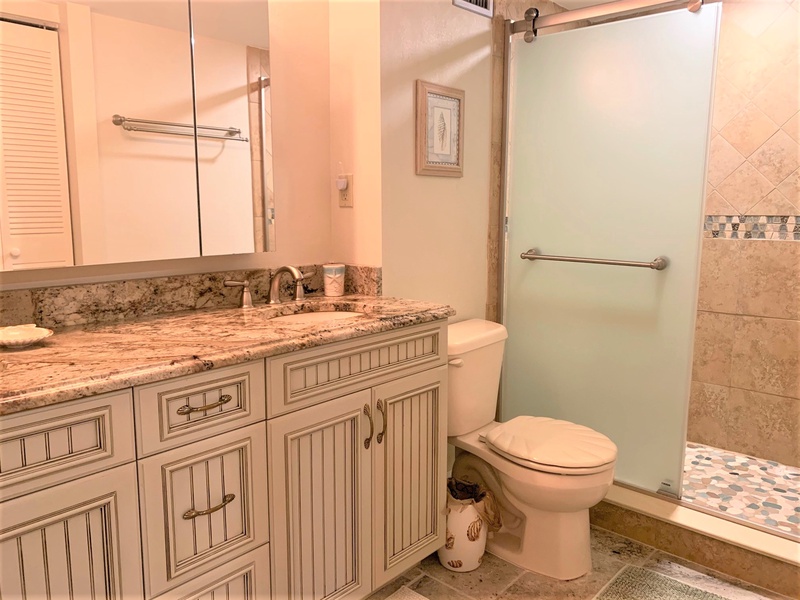 Unwind in your elegant bathroom featuring granite countertops, a glass-enclosed shower, and charming coastal details that make getting ready a pleasure.