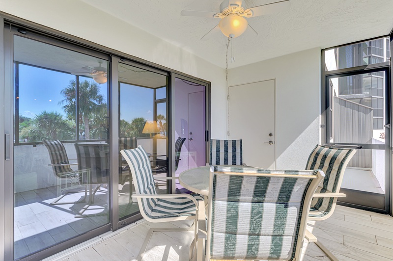 Relax in your bright, airy sunroom where striped chairs invite you to unwind with views of tropical palms through floor-to-ceiling windows.