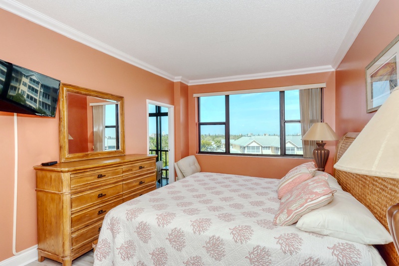 Rest in your bright, coral-toned bedroom with stunning views and warm wood furnishings creating the perfect coastal retreat.