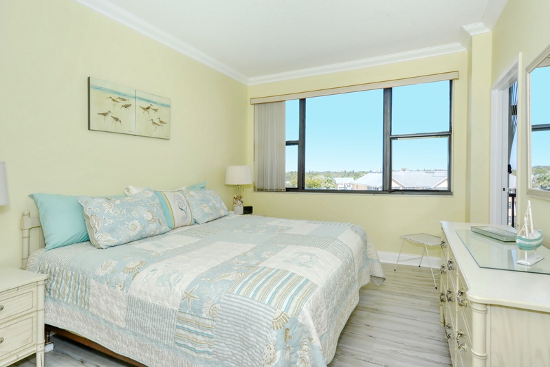 Drift off to sleep in your serene coastal-themed bedroom with soft blue linens and peaceful views through large windows.