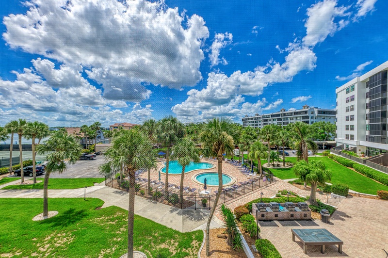 Resort property featuring tropical landscaping with palm trees, swimming pool facilities, and modern buildings under clear blue skies.