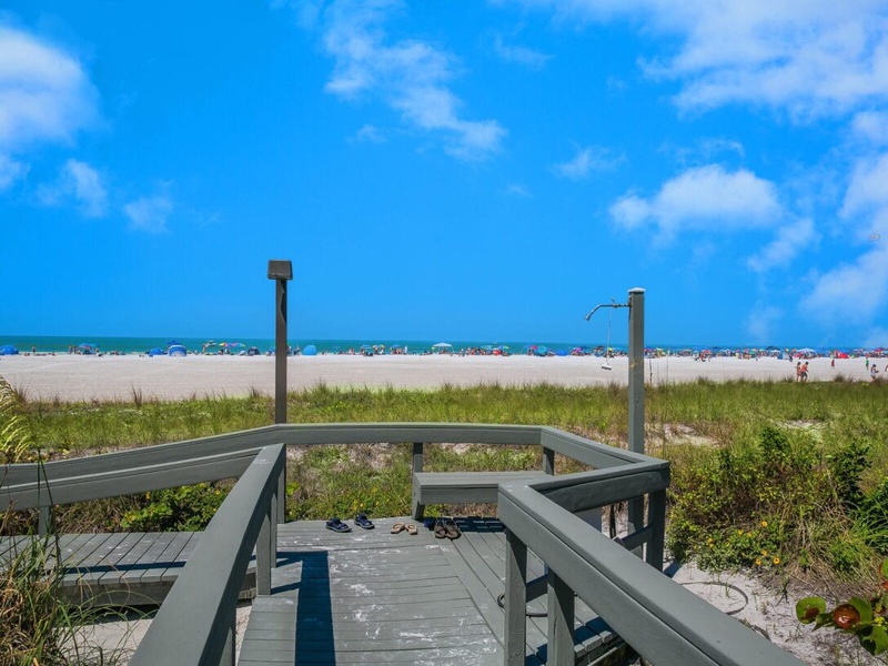 Sandy beach access with outdoor shower station leading to pristine shoreline and crystal blue waters.