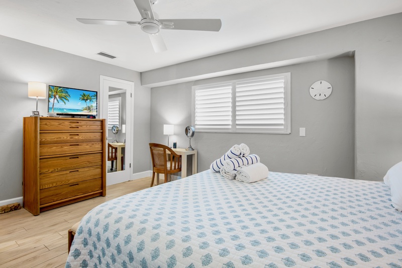 Drift off in your coastal-inspired bedroom featuring soft linens, warm wood furniture, and a peaceful ceiling fan breeze.