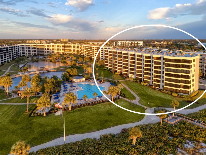 Aerial view of a resort complex featuring multiple buildings, swimming pool, and waterfront amenities surrounded by palm trees and landscaped grounds.