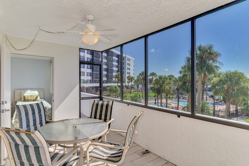 Your screened balcony offers comfortable dining with stunning pool and palm views, plus a cozy bedroom just steps away.