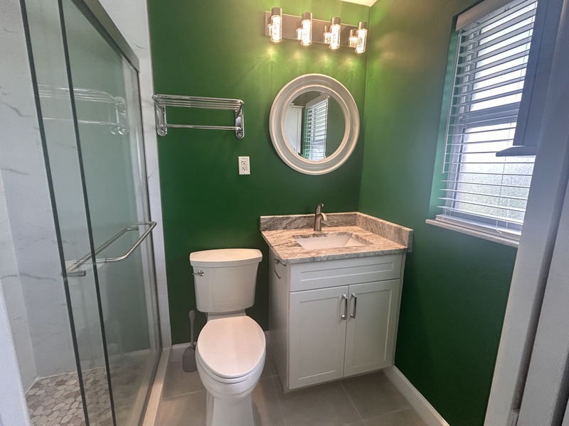 Refresh in your modern bathroom with vibrant green walls, marble vanity, and spacious glass shower.
