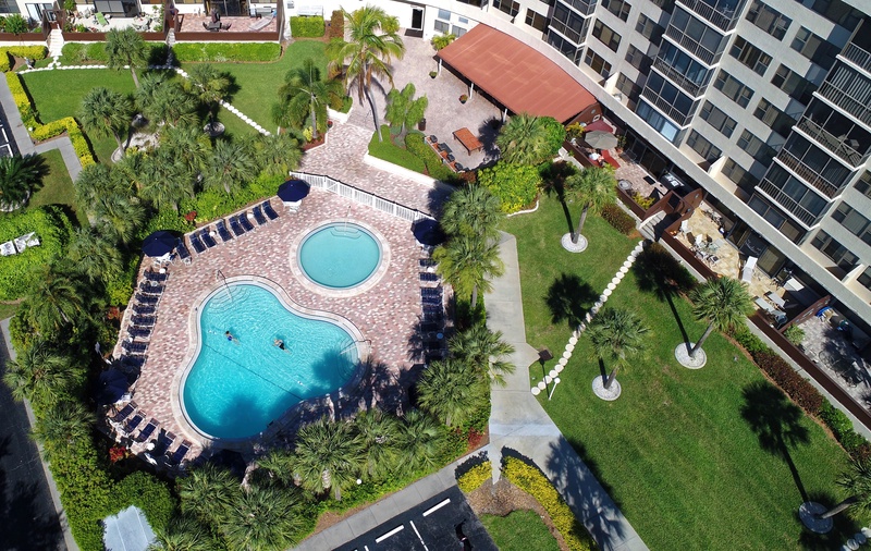 Aerial view showcasing the resort-style pool area with tropical landscaping, surrounded by modern apartment buildings and lush green spaces.