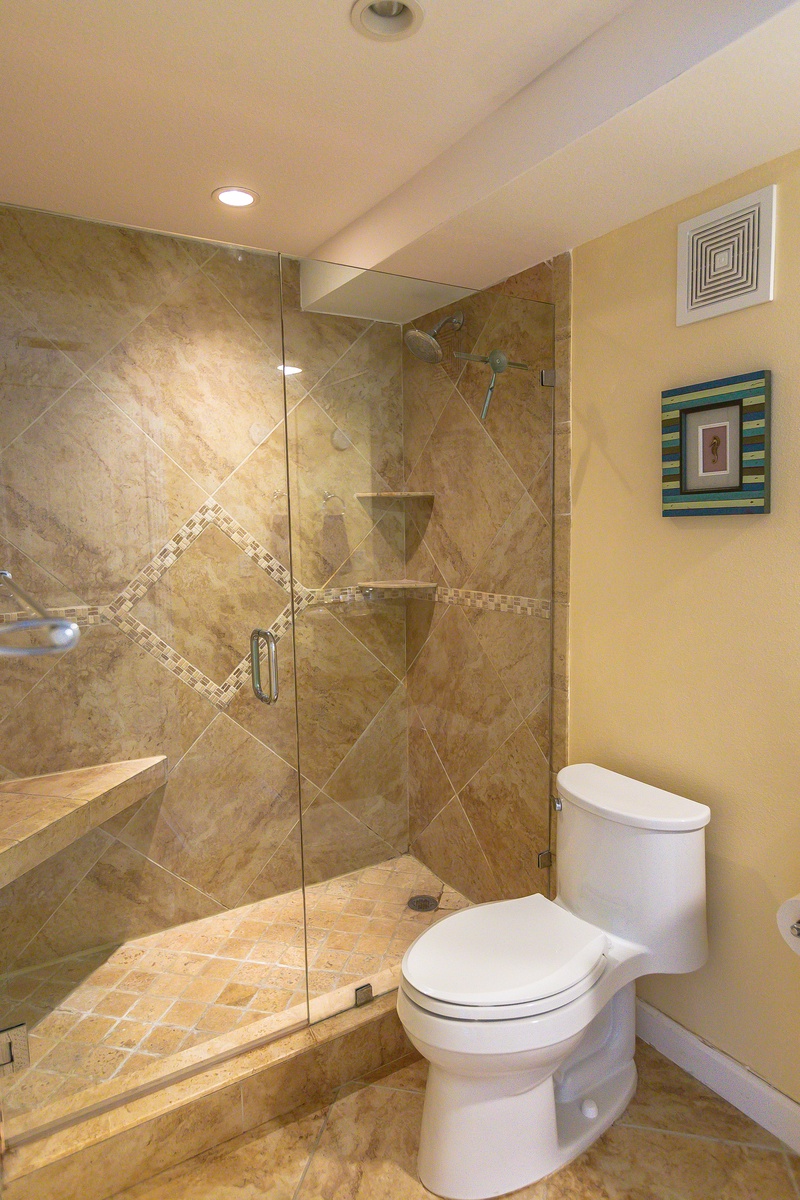 Step into your spa-like bathroom with elegant stone tile shower featuring built-in shelving and glass doors for a luxurious bathing experience.