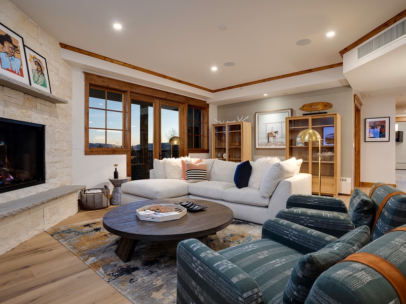 Sink into plush seating by the stone fireplace, where warm wood tones and soft lighting create your perfect evening retreat. Scenic windows frame stunning views, inviting you to unwind in comfort.