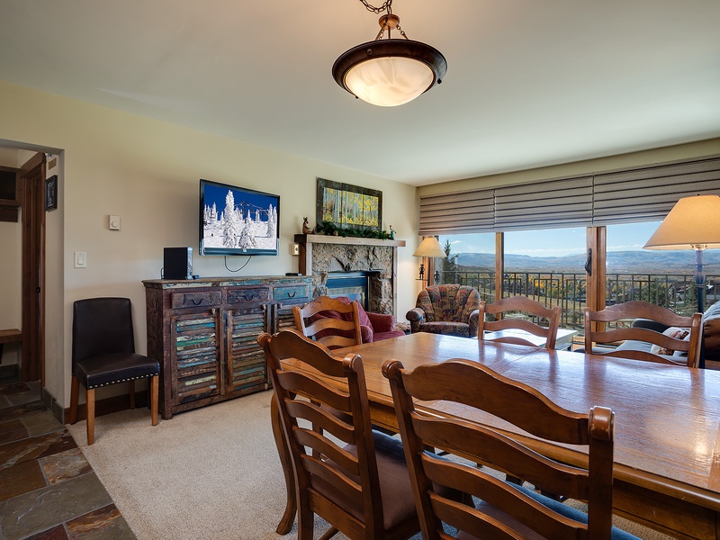 Gather around the rustic wooden table with mountain vistas stretching beyond your balcony. Cozy seating, a warm fireplace, and a TV create the perfect retreat after your adventures.