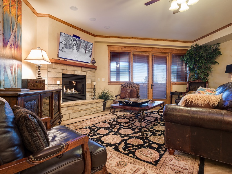 Sink into plush leather sofas by your crackling fireplace, where warm wood tones and mountain artwork create the perfect retreat after a day exploring.