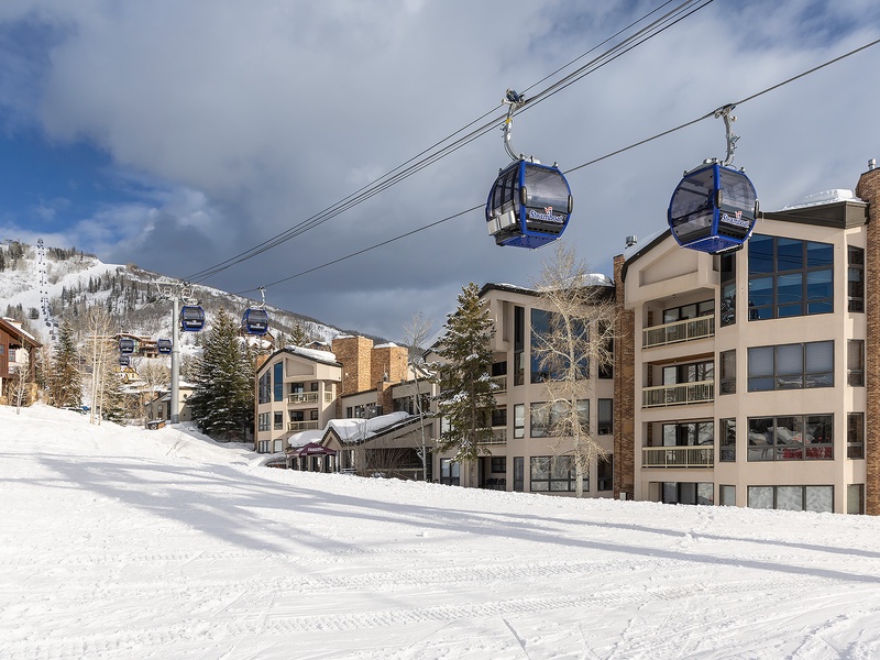 The property sits at the base of a ski resort with gondola access directly above the multi-story residential buildings, surrounded by snow-covered slopes and winter mountain scenery.