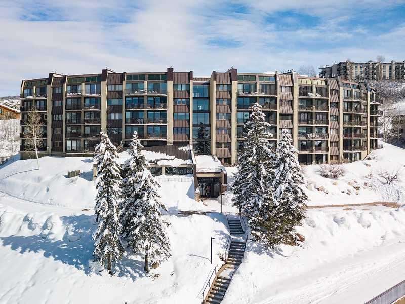 A modern mountain property set in a pristine winter landscape with snow-dusted evergreens and ski-in access, surrounded by neighboring resorts and hillside vistas.