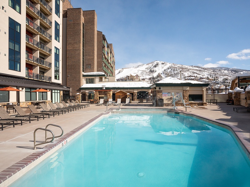 Property features an outdoor heated pool surrounded by lounge chairs, with direct ski slope access and stunning mountain views in the heart of the resort area.