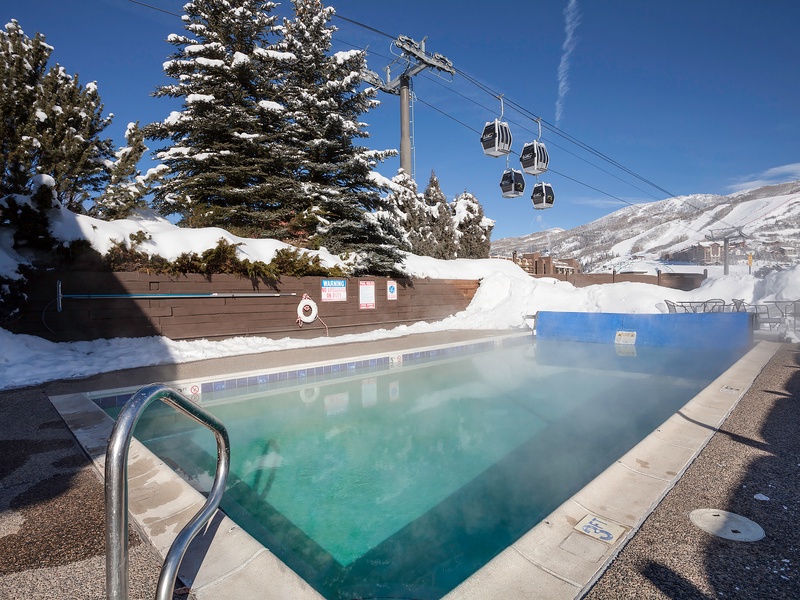 Heated outdoor pool nestled in a snowy mountain resort, surrounded by alpine trees and gondolas overhead—a tranquil spot after a day on the slopes.