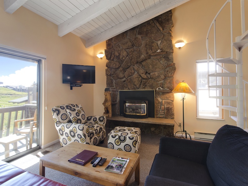 Relax in your cozy living room with vaulted ceilings, a striking stone fireplace, and sweeping views of rolling hills from your private balcony.