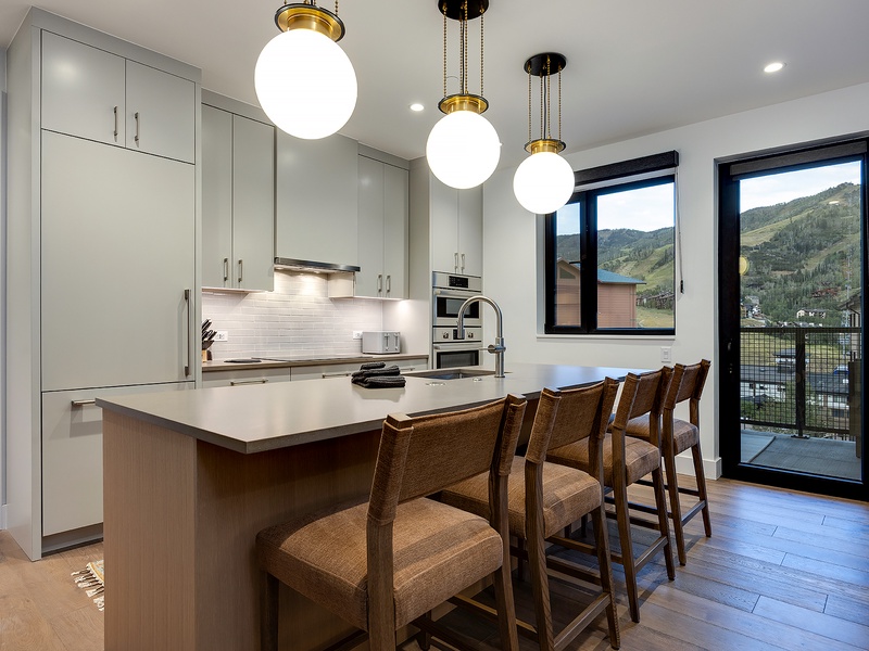 Your modern kitchen glows with natural light, where a spacious island with seating invites casual meals while you take in stunning mountain vistas through large glass doors.