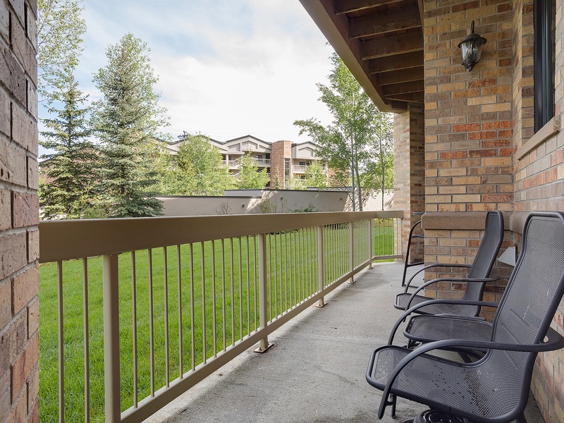 A private outdoor balcony awaits with two comfortable mesh lounge chairs overlooking lush green lawns and mature trees, perfect for your morning coffee or evening relaxation.