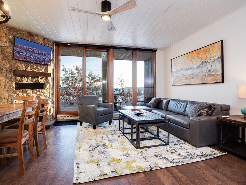 Relax in your open-concept living space with soaring ceilings, a cozy stone fireplace, and large glass doors framing stunning mountain views—your perfect retreat after a day of adventure.