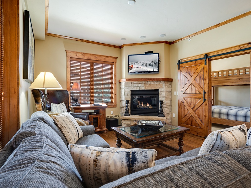 Curl up on plush sofas beside your own stone fireplace, where rustic wood accents and a cozy bunk nook create the perfect mountain retreat for relaxing after adventure.