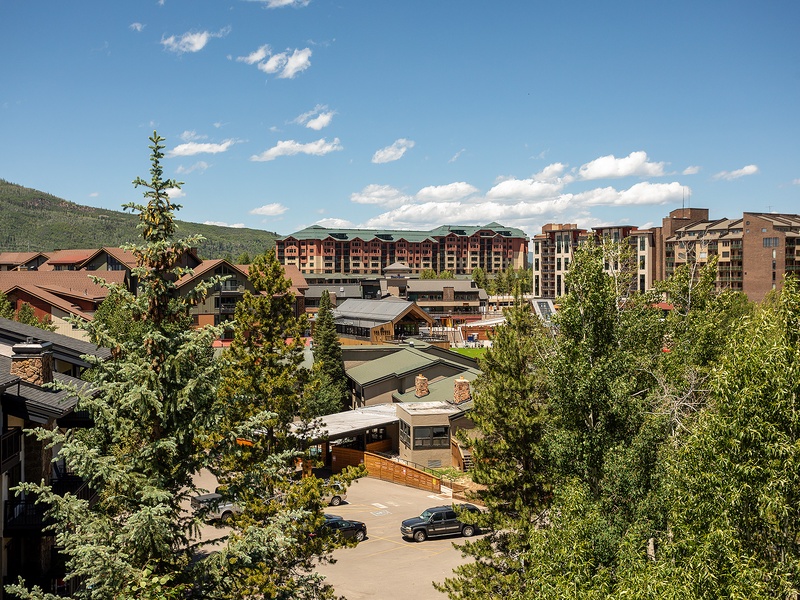 Mountain resort community nestled in a scenic valley with multi-story buildings, lush greenery, and dramatic peaks framing the village skyline.