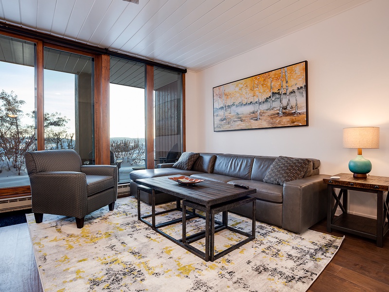 Unwind in your cozy living room with a stunning lake view framed by floor-to-ceiling windows. Sink into the plush leather sofa and let the natural light and peaceful scenery wrap you in comfort.