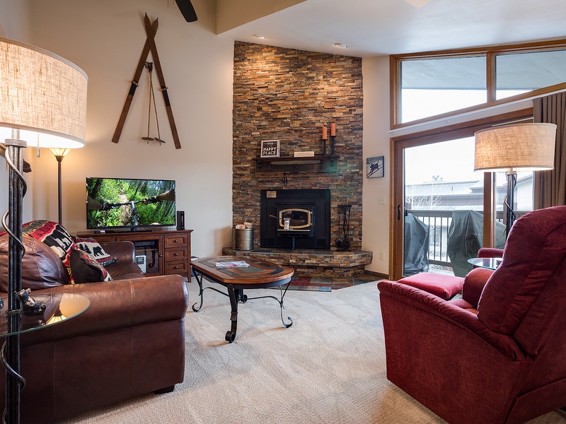 Unwind in this inviting living space with plush seating, a cozy stone fireplace, and large windows framing mountain views—your perfect retreat after a day of adventure.