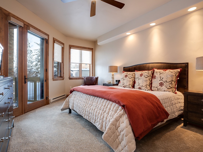 Unwind in your serene bedroom featuring a plush bed with elegant linens, warm lighting, and a private balcony door framing peaceful winter views for ultimate relaxation.
