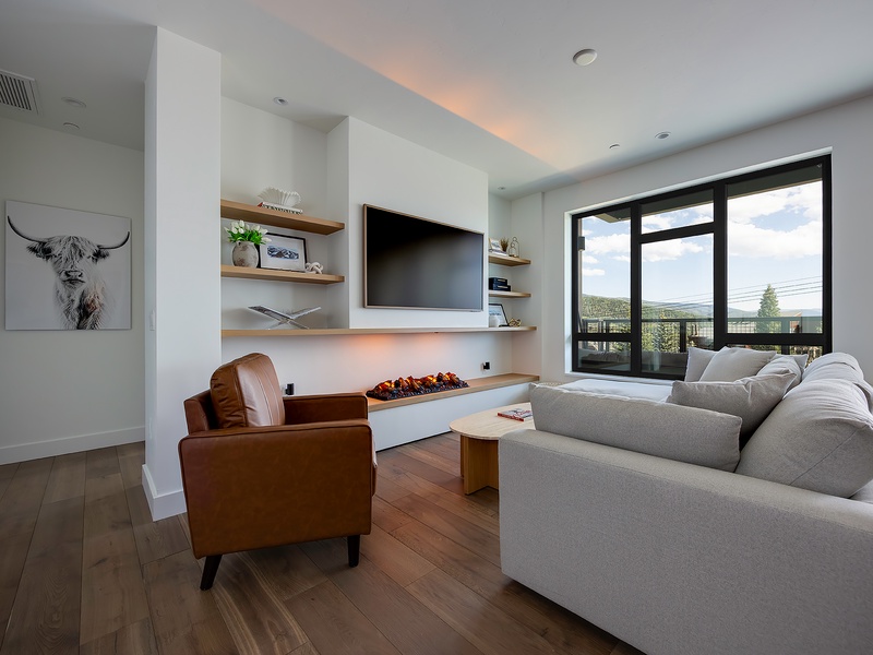 Sink into your cozy living room where a modern fireplace warms the space, and expansive windows frame the surrounding landscape. Unwind with your favorite shows or simply take in the peaceful setting just outside.