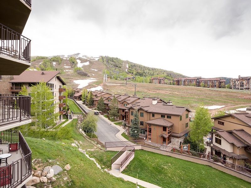 Mountain resort community nestled at the base of ski slopes, featuring residential buildings surrounded by spring greenery and remnants of winter snow on the hillside.