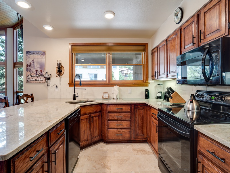 Your fully equipped kitchen features rich wood cabinetry, granite counters, and modern black appliances—perfect for preparing hearty mountain meals after a day exploring Steamboat Springs.