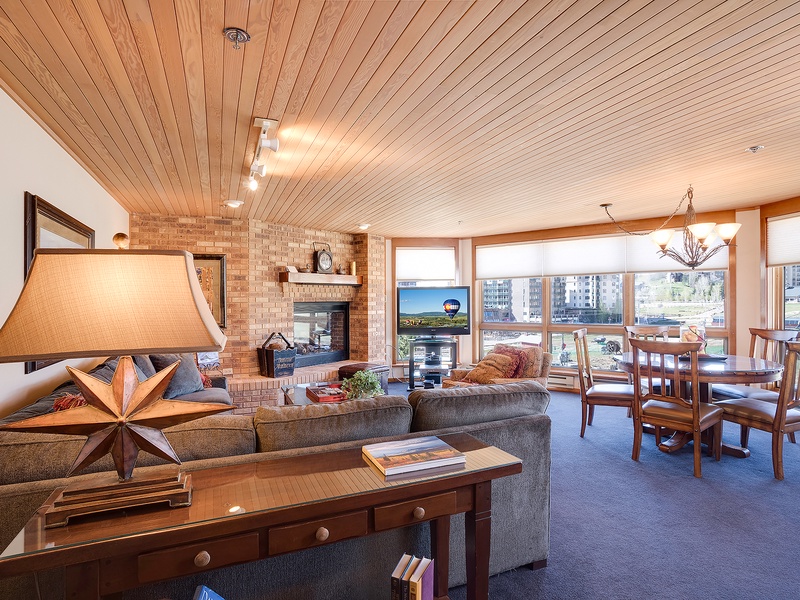 Unwind in your spacious living area with warm wood ceilings, cozy fireplace, and panoramic water views framing every moment of relaxation and togetherness.