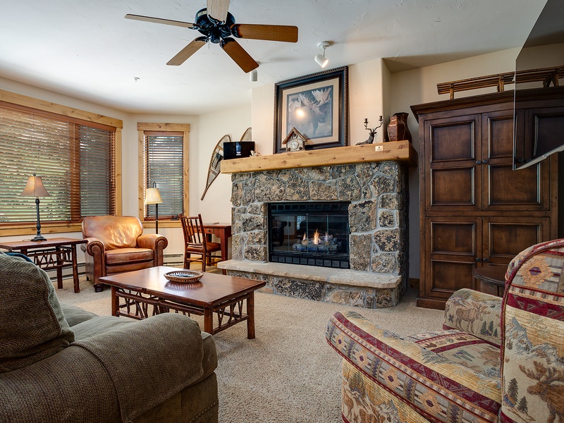 Unwind in your cozy living room with a crackling stone fireplace, comfortable seating, and warm wood furnishings perfect for mountain getaways.