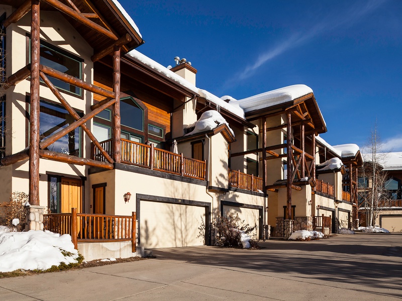 Charming mountain townhomes with rustic timber accents and private balconies, nestled in a peaceful winter setting under bright blue skies.