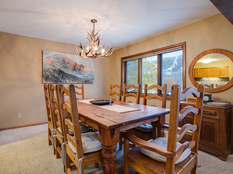 Gather around this rustic dining table with mountain views just beyond your window. The antler chandelier and warm wood tones create a cozy alpine atmosphere perfect for memorable meals together.