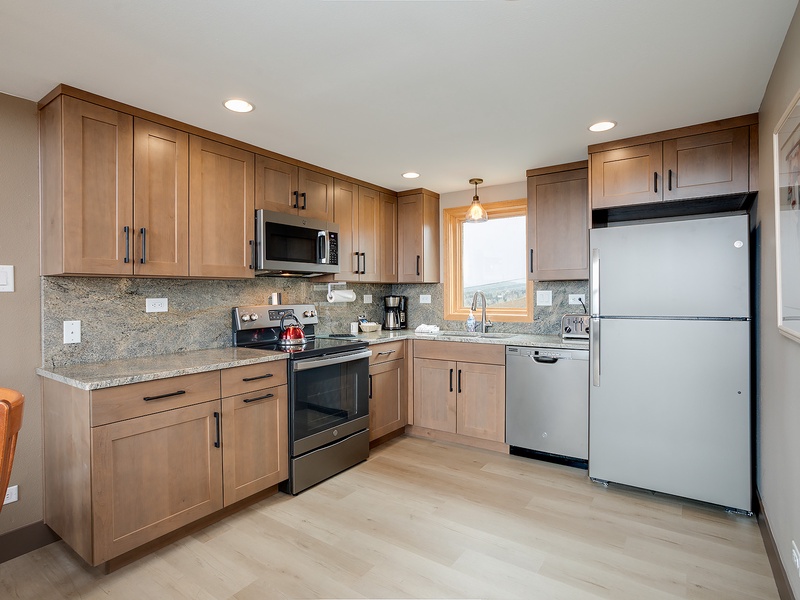 Your fully equipped kitchen features warm wood cabinetry, granite countertops, and modern stainless appliances—perfect for preparing meals while enjoying natural light and mountain vistas through the window.