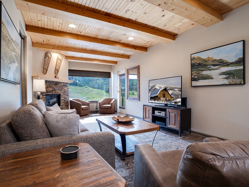 Unwind in your spacious living room, where exposed beam ceilings and a cozy stone fireplace create a mountain retreat atmosphere. Sink into plush seating while enjoying scenic views through expansive windows.