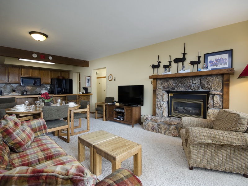 Settle into your cozy living space where a crackling stone fireplace and plush seating await. The open layout connects your kitchen and living areas for effortless gathering.
